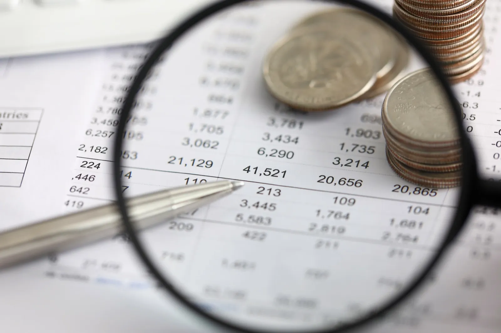 Finanzielle Kennzahlen unter einer Lupe mit Stift und Münzstapel